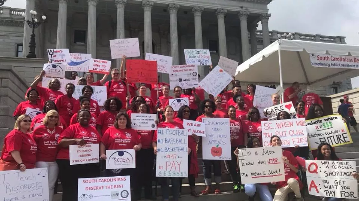 Teachers stand in front of the South Carolina statehouse dressed in red with signs demanding fair funding