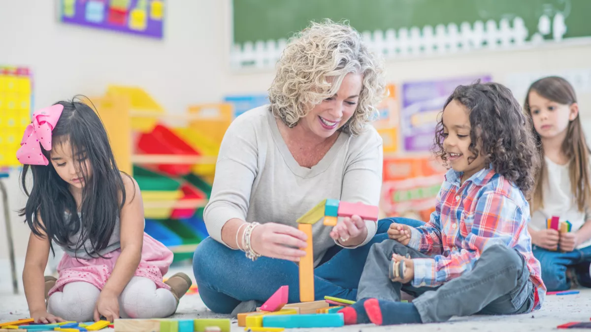 A smiling pre-k teacher and students use blocks as they learn.