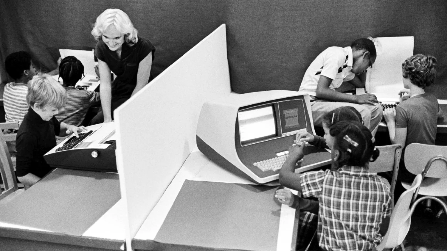 Computer room from the 1980s with diverse students and a white female teacher.
