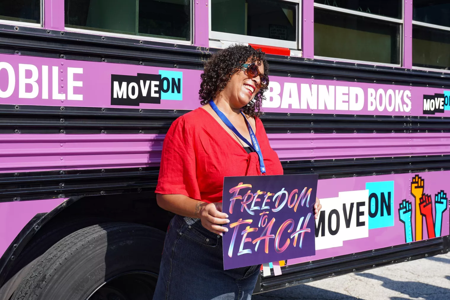 Woman stands in front of a purple schoolbus with a sign that says freedom to teach at the 2023 Freedom to Learn Rally in Orlando