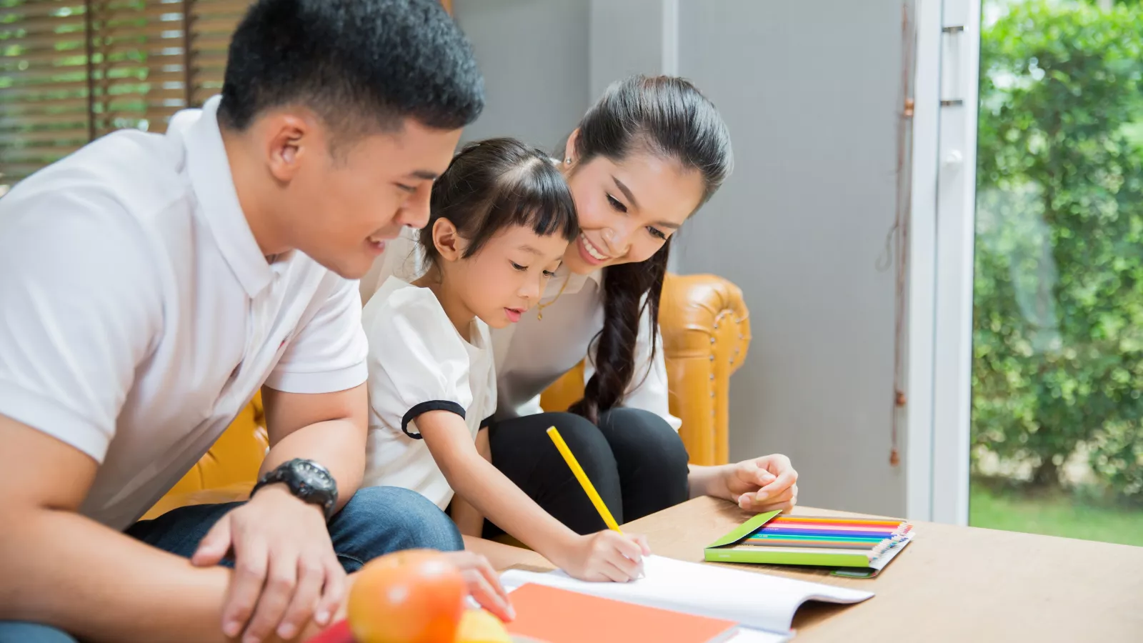 A mother and father help a child write.