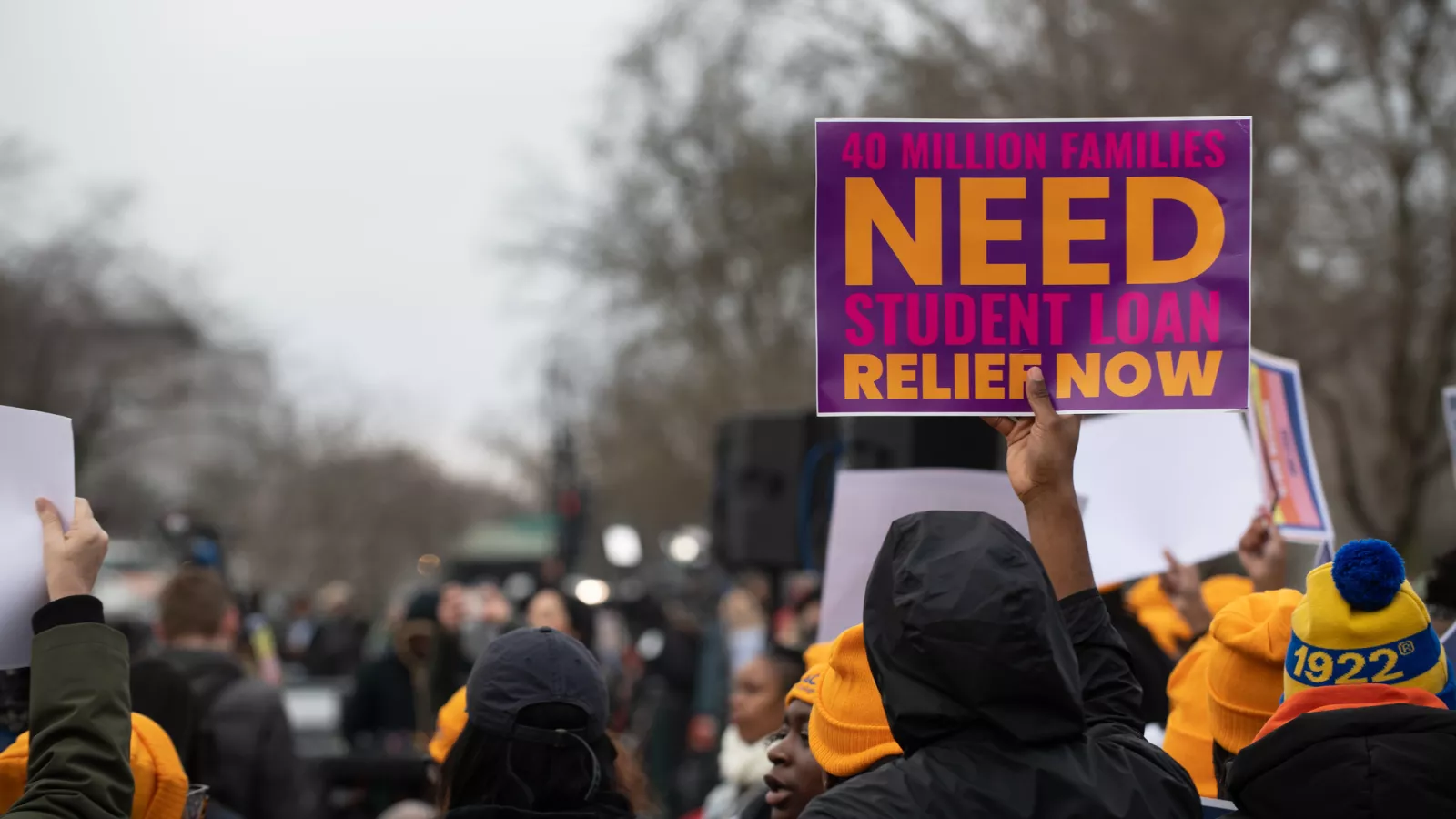 Sign held up at rally saying 40 million families need student loan relief now.