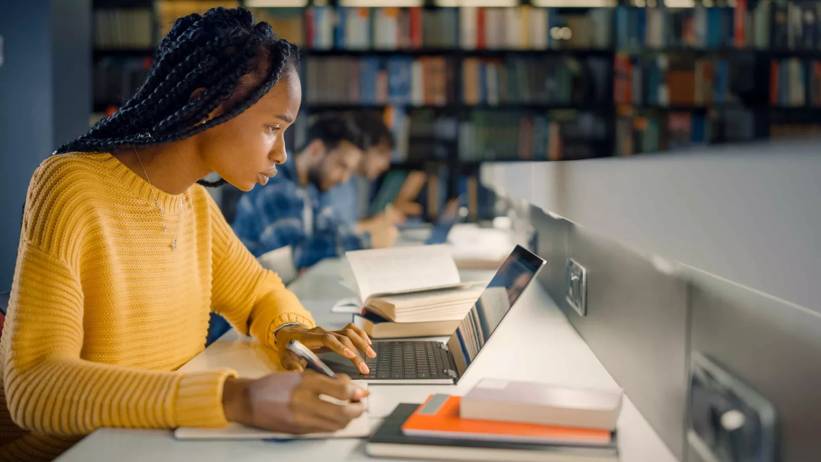 Young Black girl with braids concentrating on laptop in a library