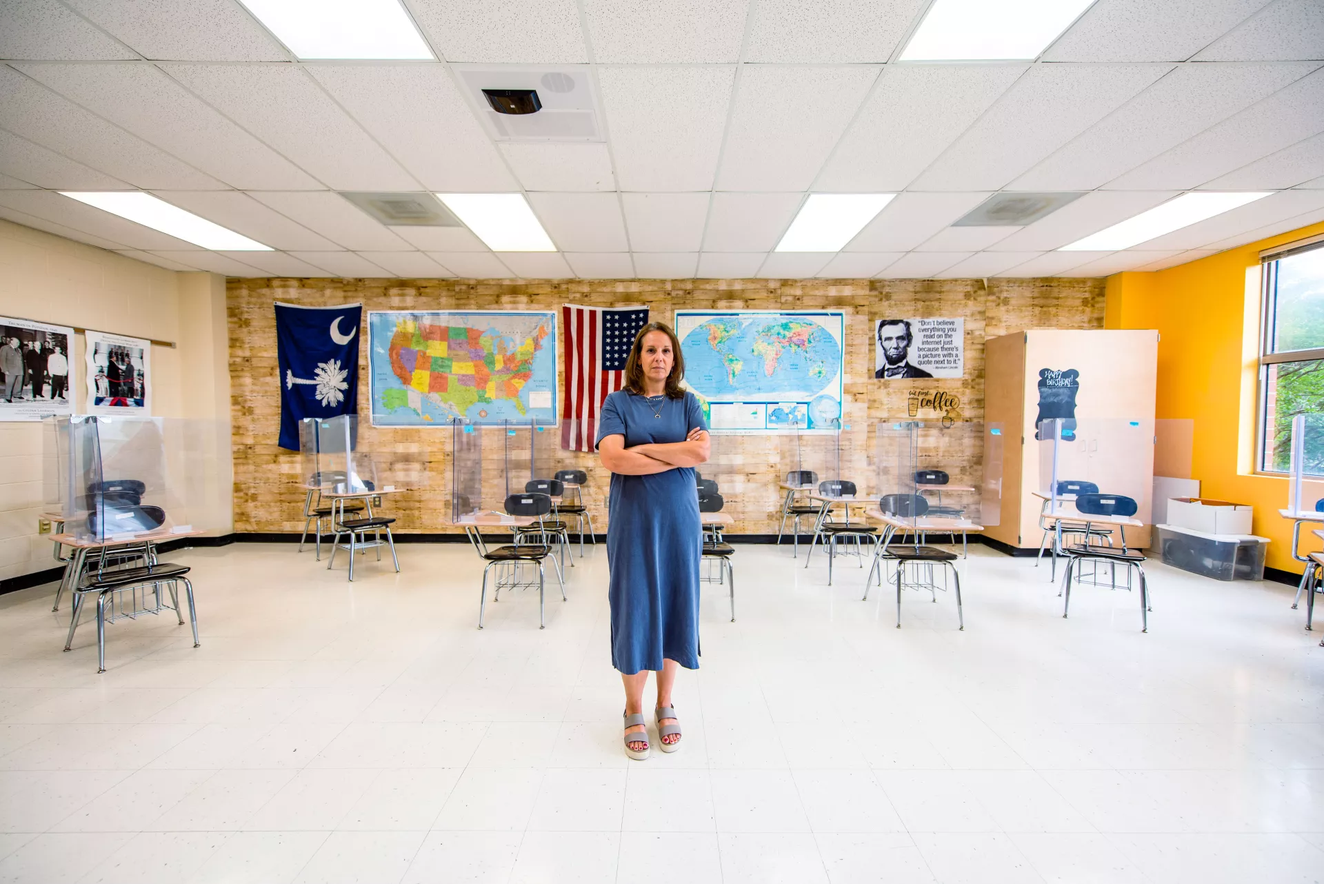 Teacher stands with arms crossed in a Social Studies classroom with plexiglass on desks.