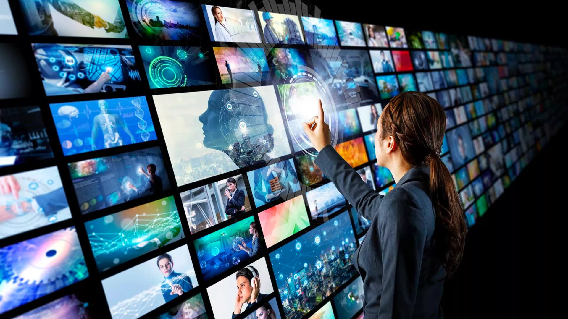 A woman stands in front of several bright screens with many images; some include things from outerspace, others are shadows of people; the woman is touching one screen.