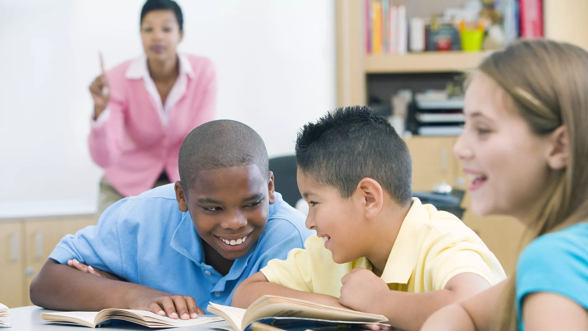 Boy students talking in class while teacher speaks to them from the background