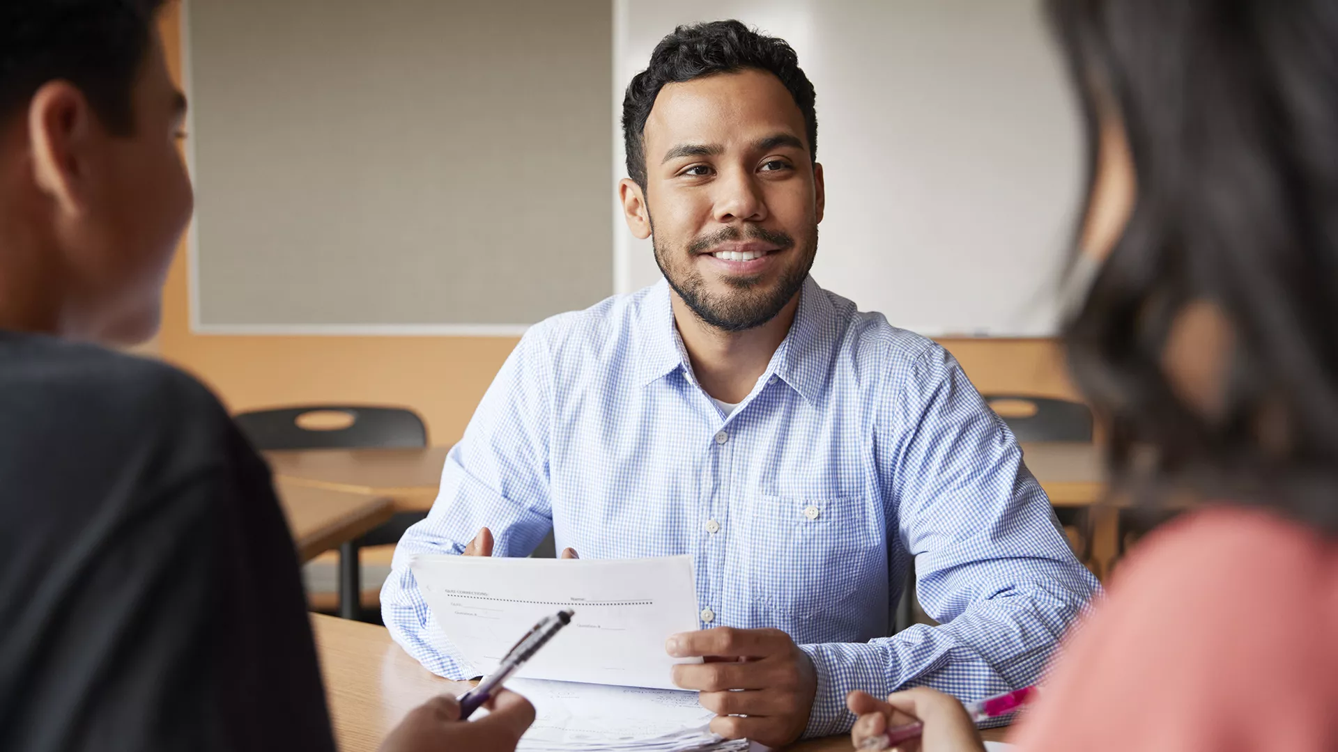 male Latino tutor talks to parents at a school