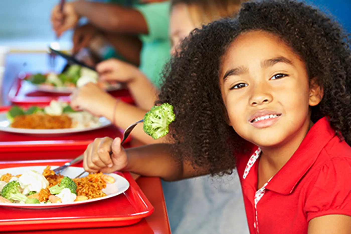 Smiling public school girl eating healthy vegetable lunch