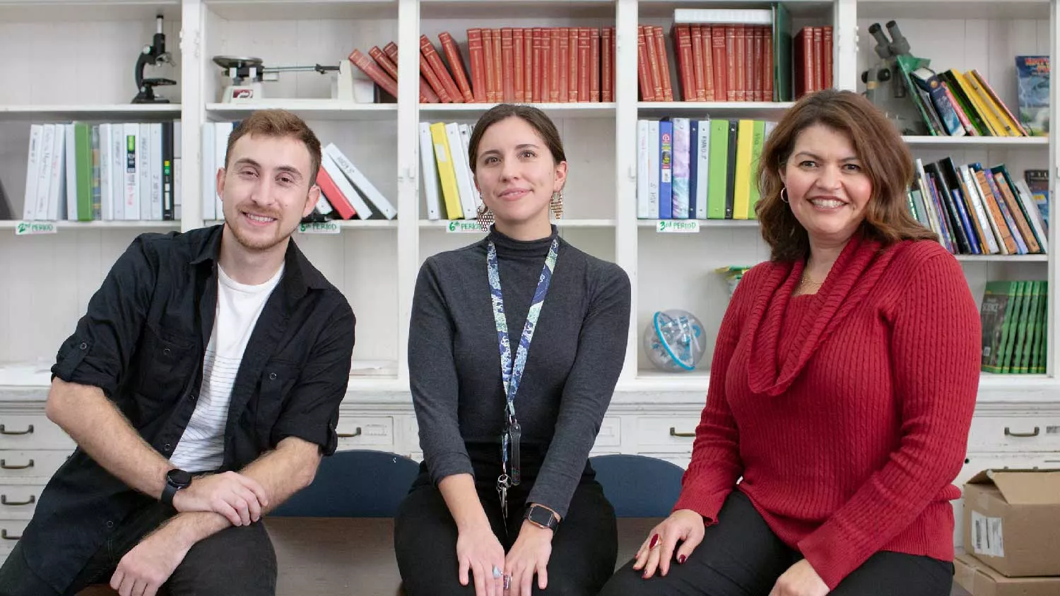 Resident Jaime Vazquez, science teacher Cecilia Frisardi, and Director of Clinical Education Esther Jamarillo-Woo smiling and sitting in front of books.