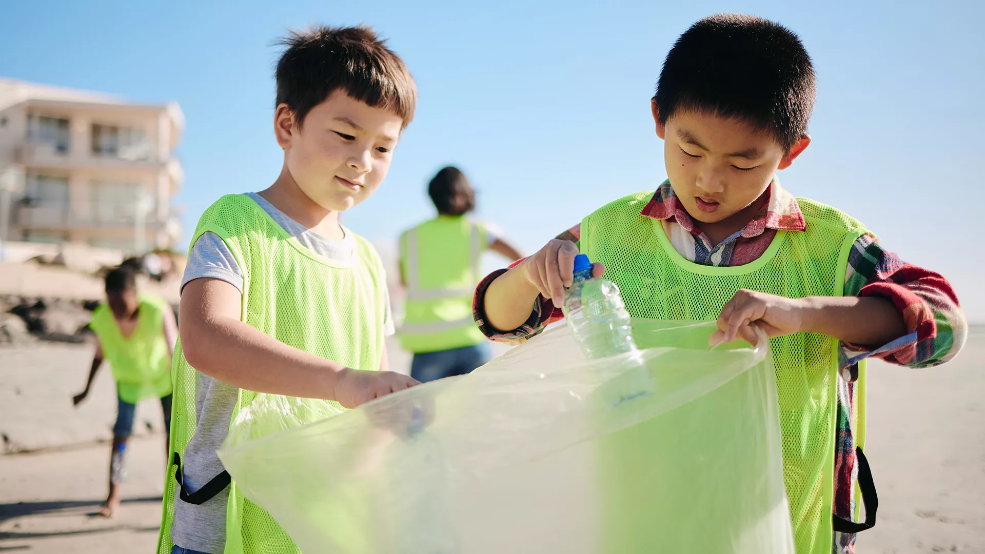 two young boys pick up trash on a sunny beach