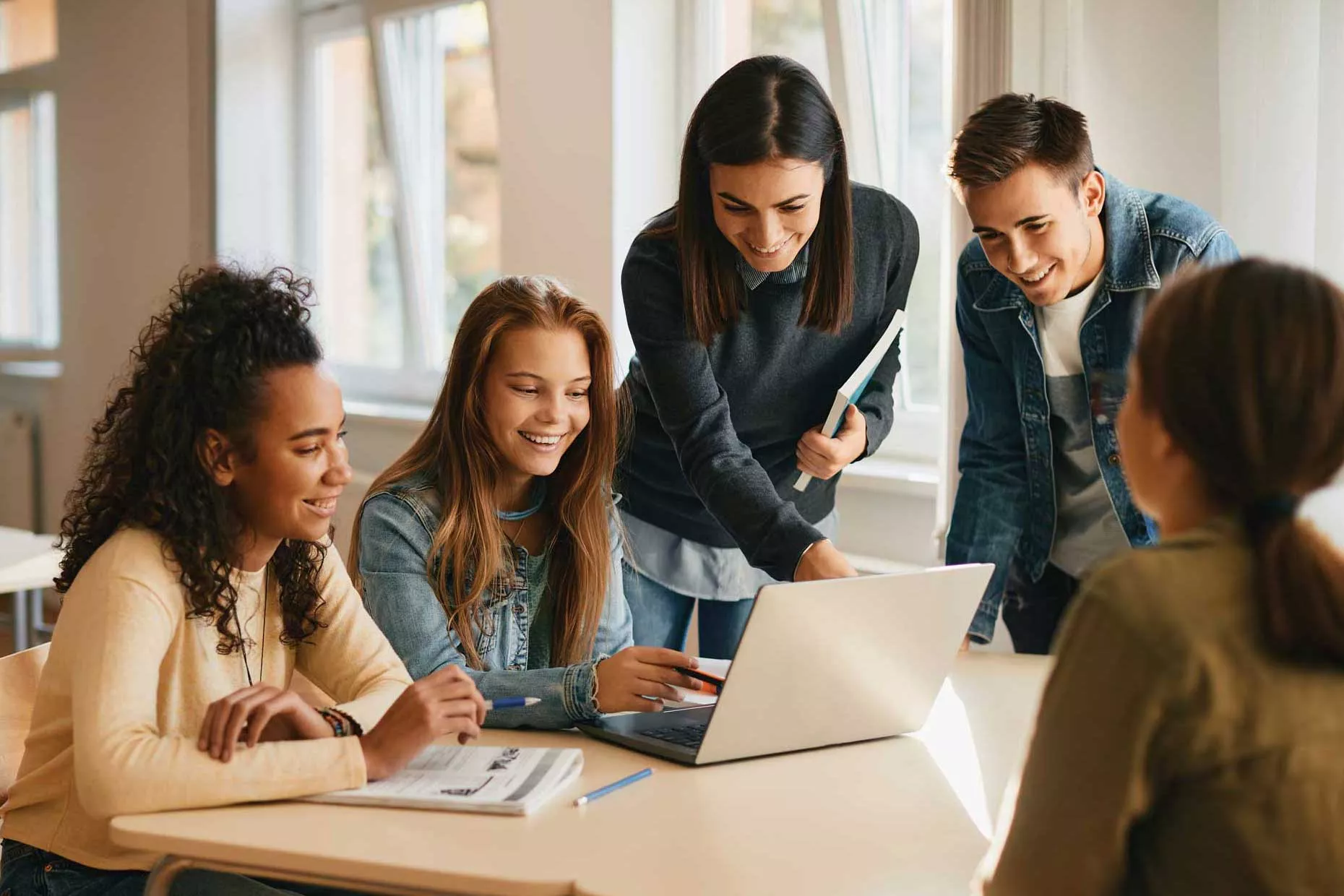 Students and teacher looking at laptop on desk.