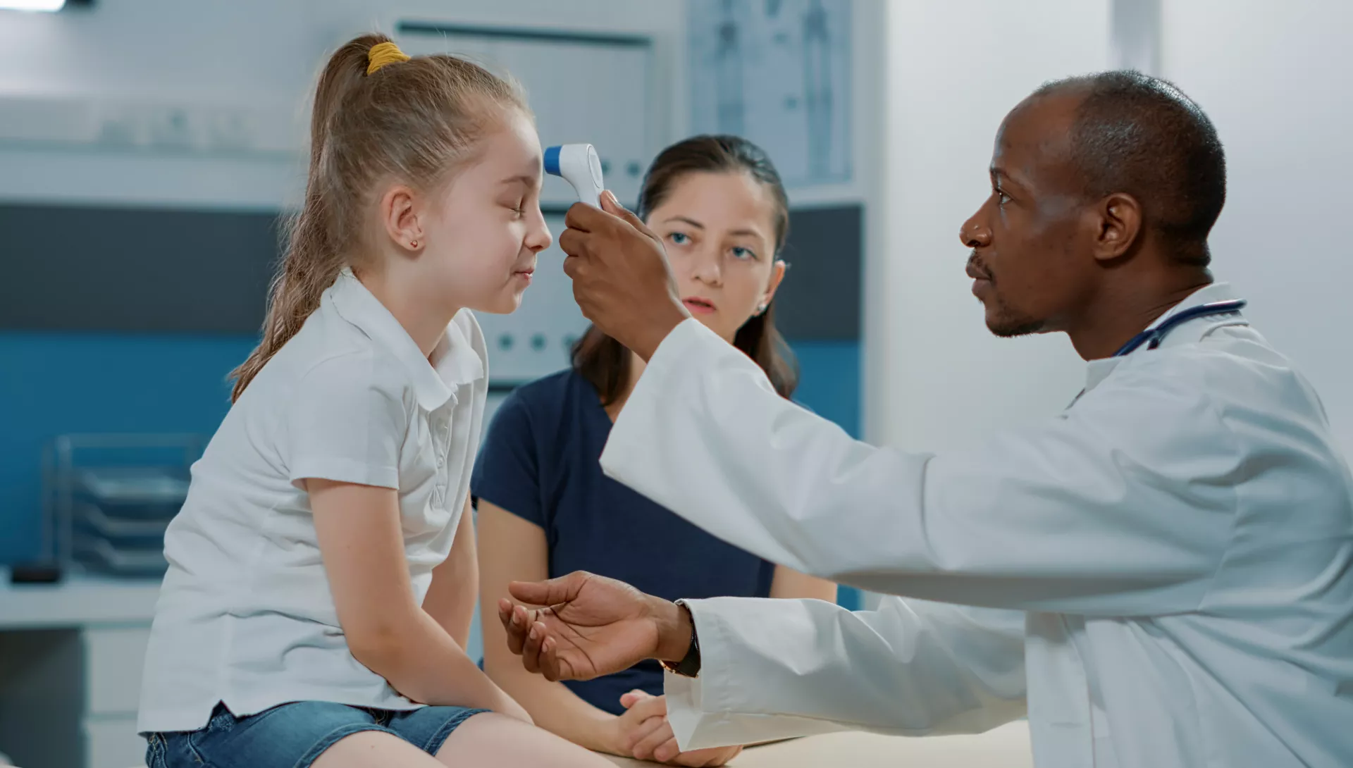 Doctor taking girl's temperature as mother looks on.