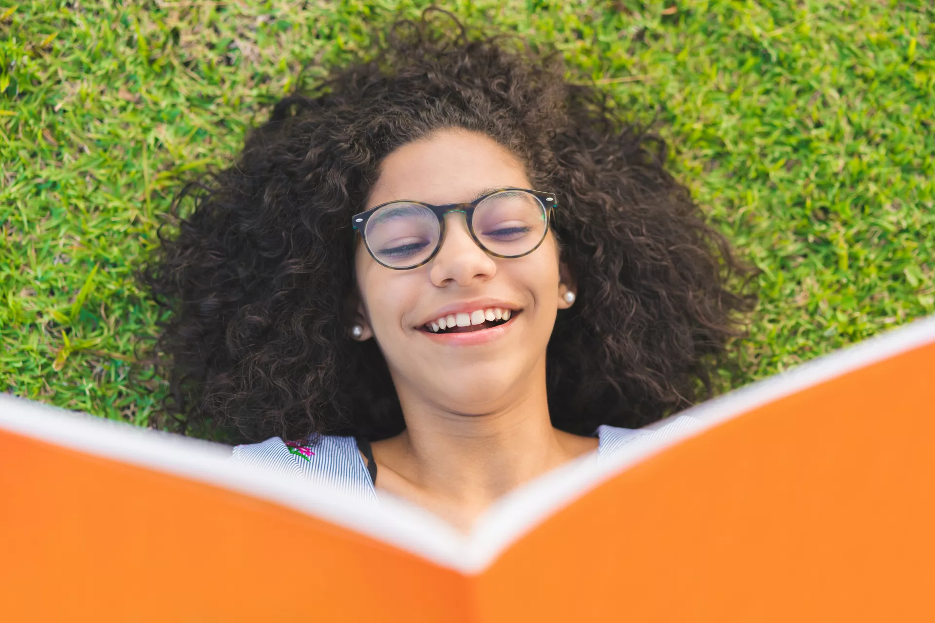 A girl reads a book while lying in the grass