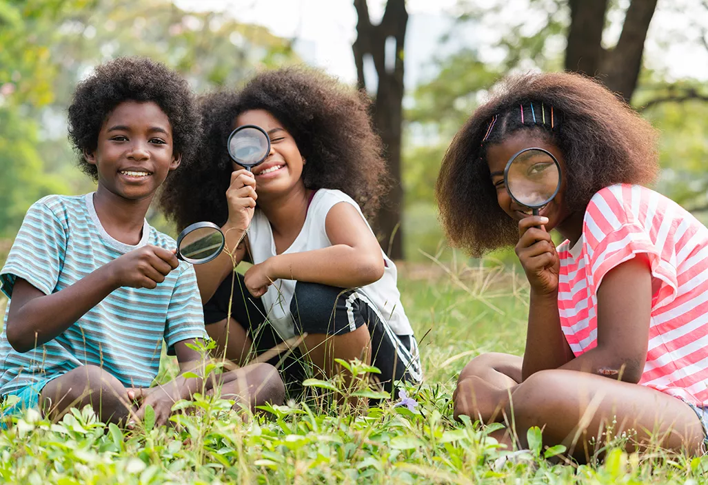 Children experimenting with magnifying glasses in a grassy field