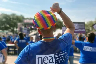 An NEA member in a rainbow hat raises his fist