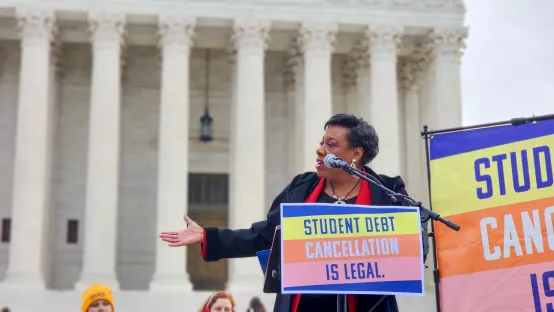 Photo of Becky Pringle speaking in front of the Supreme Court with student debt signs around her