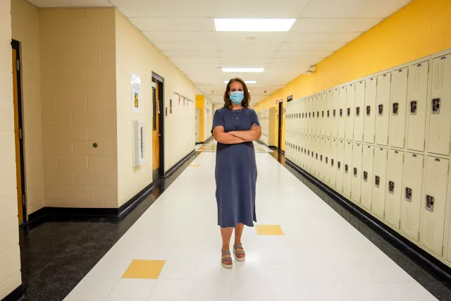 Teacher with mask stands in hall, arms folded