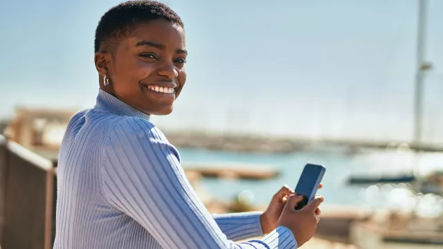 Black woman leaning on railing and texting on her mobile phone
