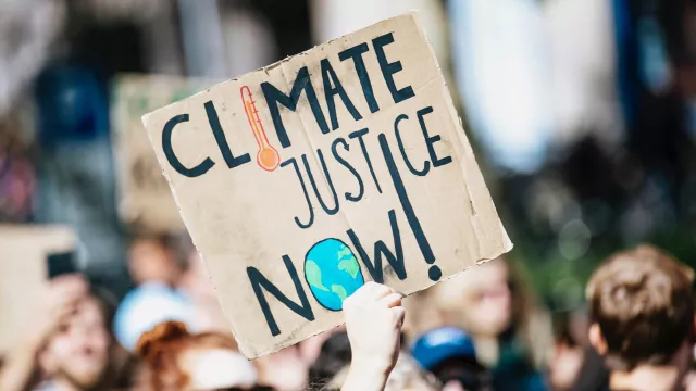 Protestors holding a carboard sign in a crowd that says Climate Justice Now