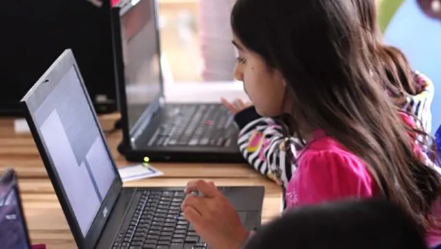 A young girl writes code on a laptop