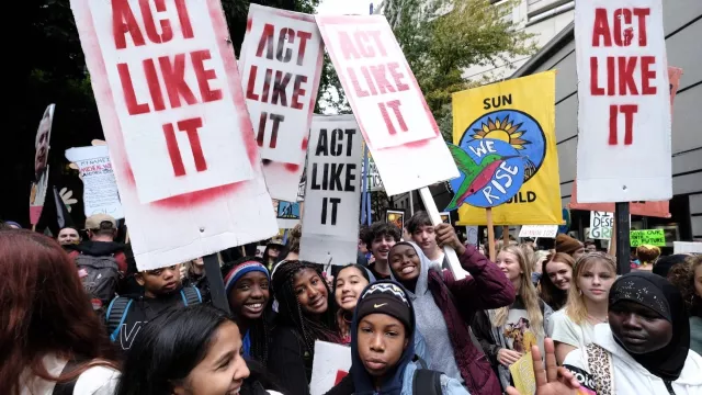 Climate activists marching with signs that read, "Act Like It"