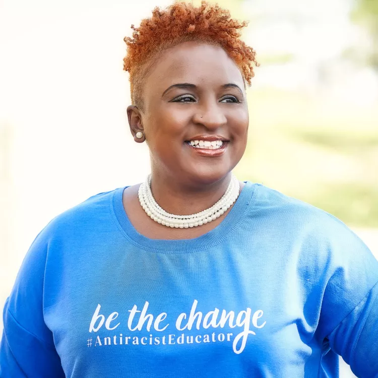 Black woman smiling and wearing a blue shirt that says "Be the change #antiracisteducator"